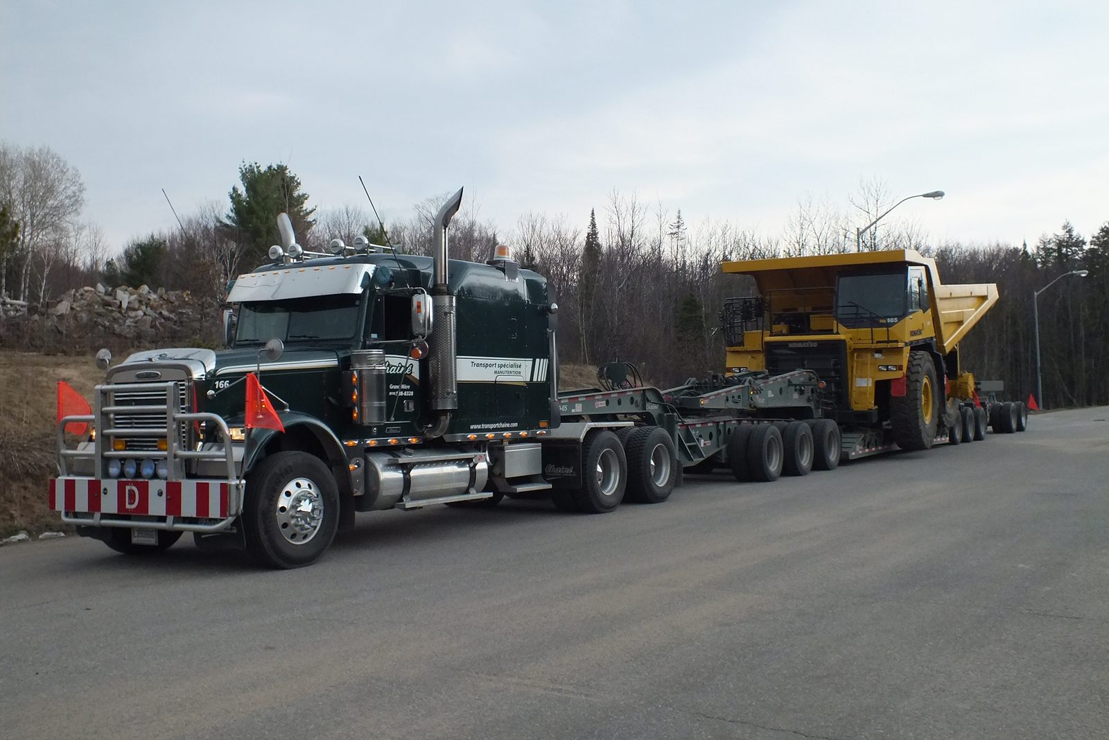 Un tracteur Chainé tirant un fardier surbaissé chargé d’une benne de camion de mine jaune
