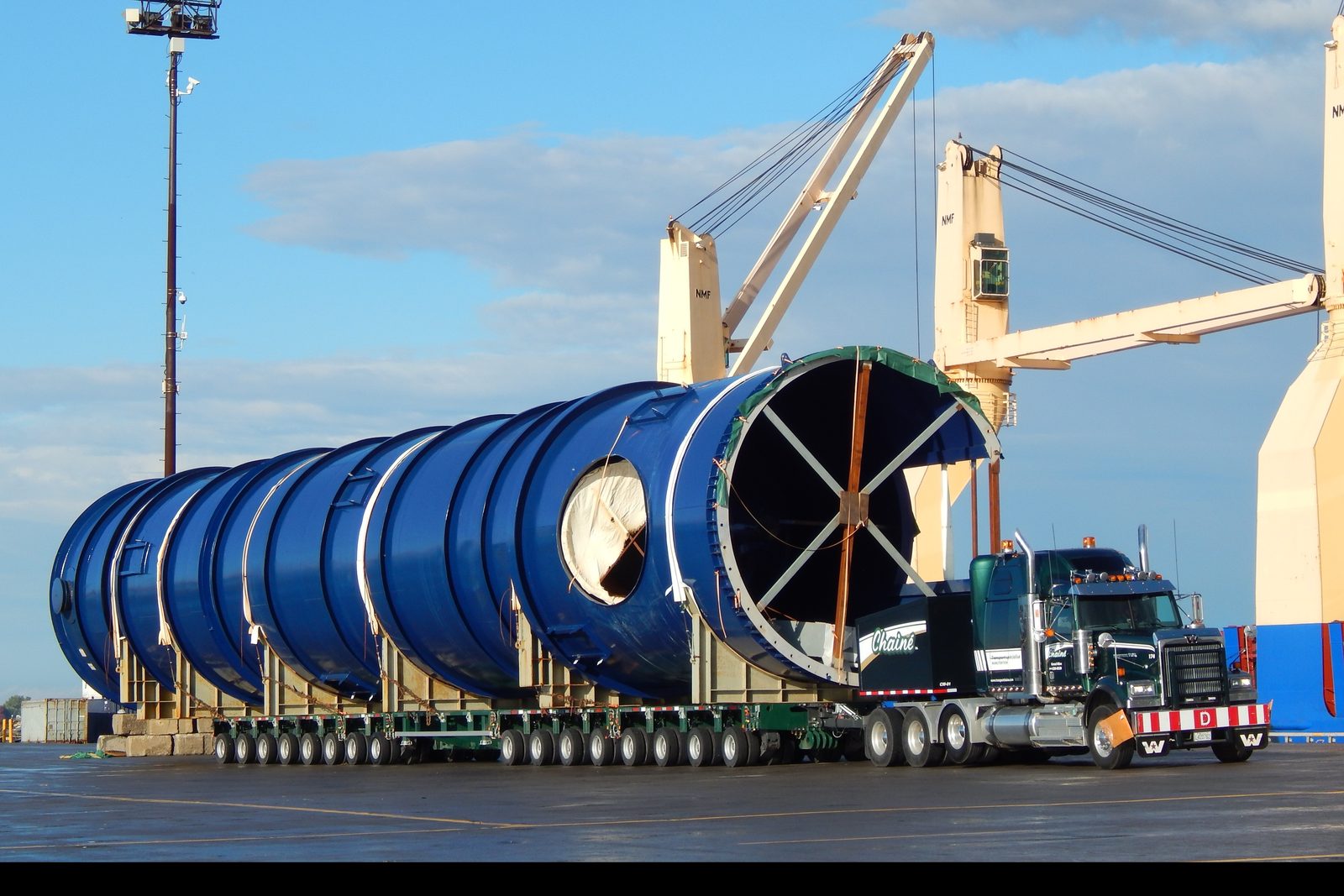 Des segments bleus de tour de refroidissement sur des modules Goldhofer, au quai du Port de Bécancour, une grue de navire au-dessus