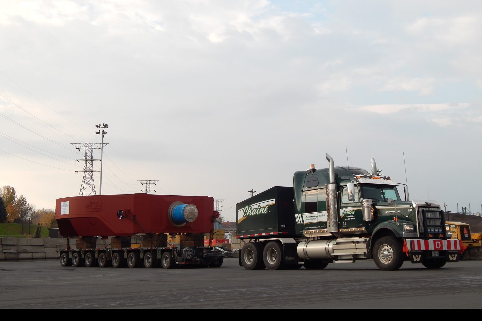 Un rotor rouge sur une remorque multi-essieux, un tracteur Chainé à côté, dans une cour industrielle