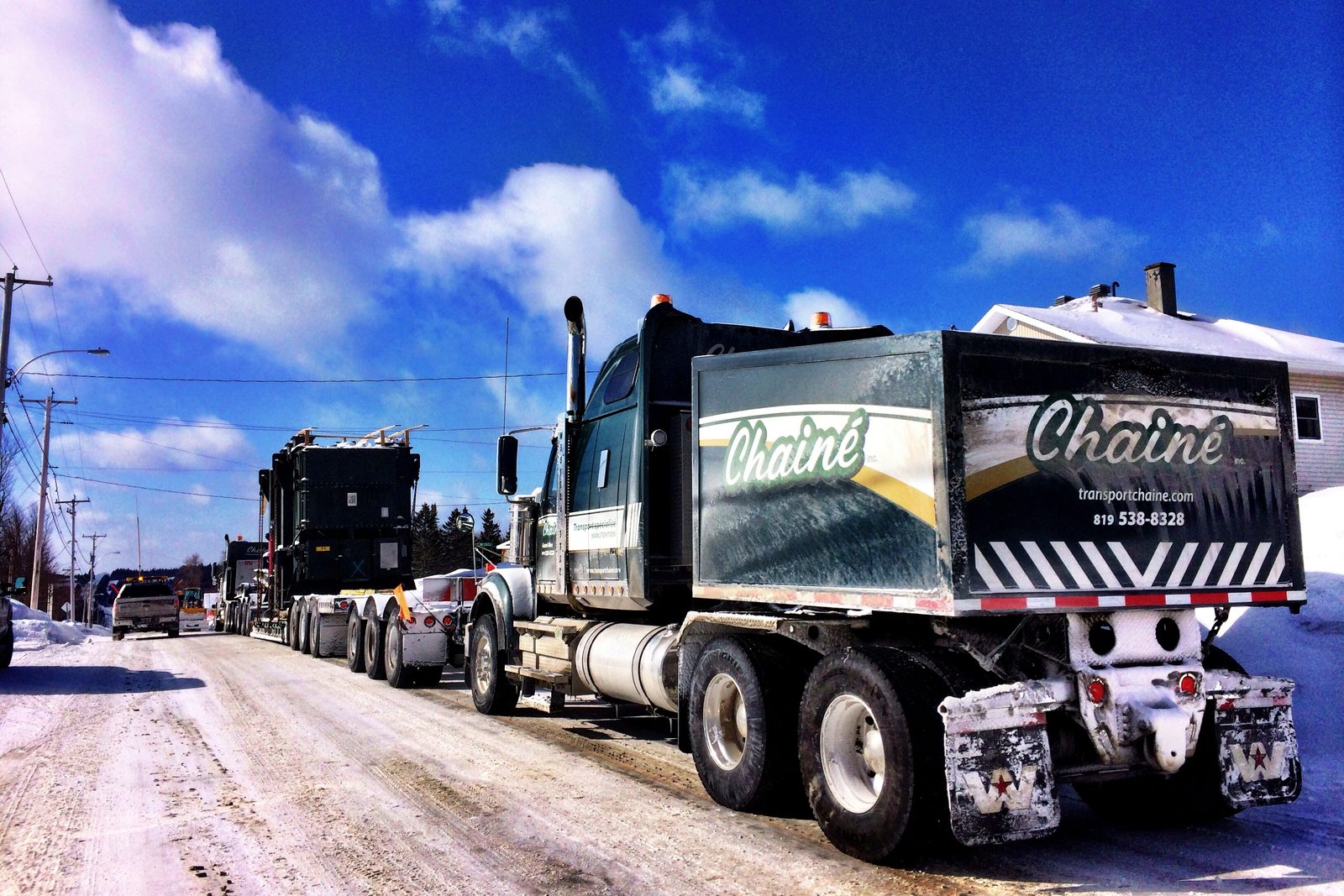 Un convoi Chainé en hiver : le tracteur et sa remorque marquée « Chainé » devant, un second convoi derrière, route enneigée et ciel bleu