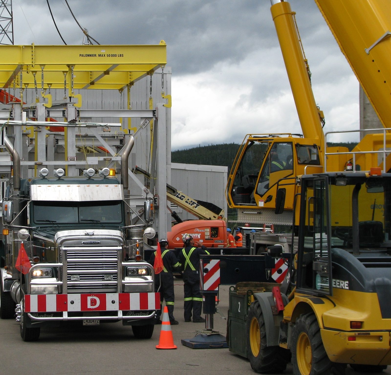 Un tracteur Chainé sous un portique de levage jaune, sur un chantier, une grue jaune à droite