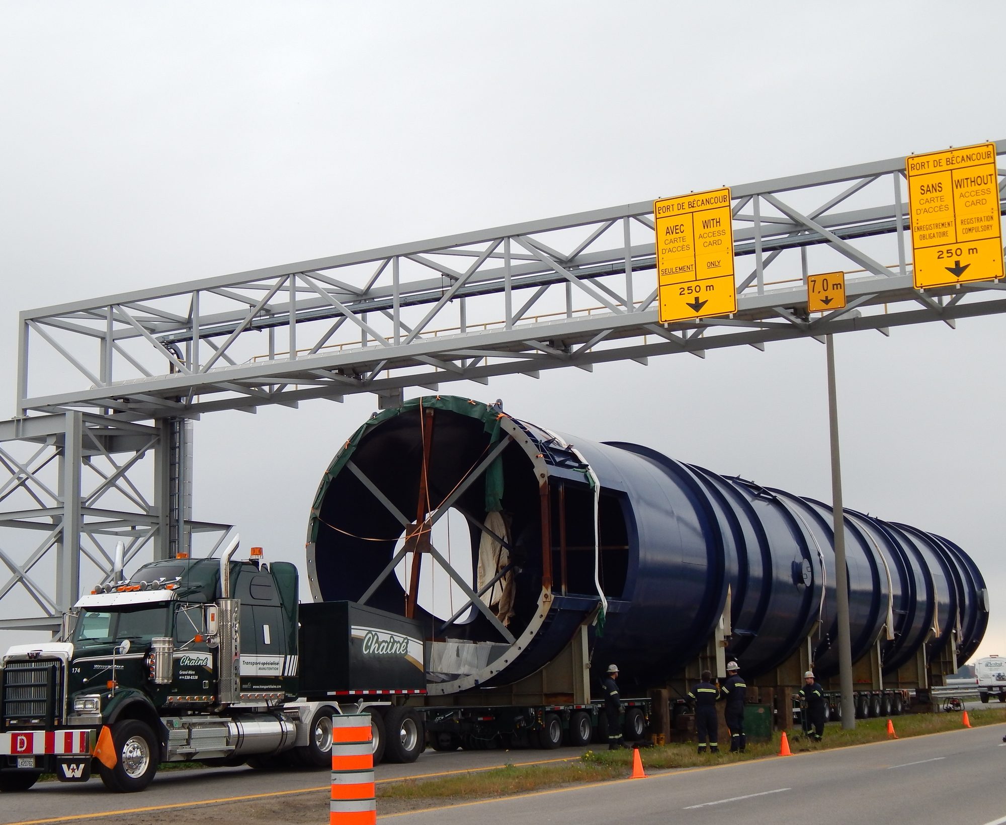 Le convoi Chainé devant le portique d’acier à la sortie du port, la tour bleue sur le transporteur, des cônes orange